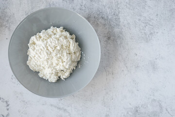 Top view of cottage cheese in a gray plate on a gray concrete background with copy space for text. Sources of calcium and protein. Concept of dairy products, healthy food, diet.