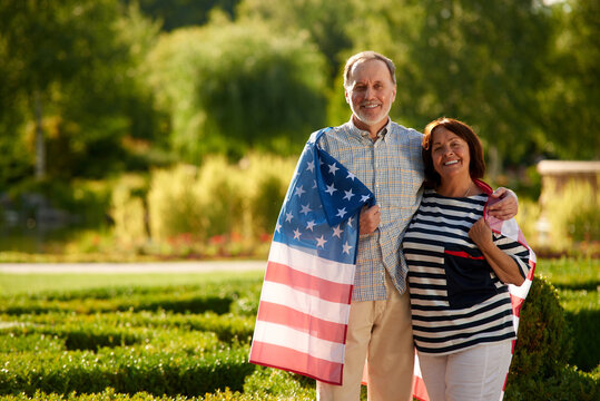 Retired couple with usa flag. man patriotic mature man woman standing in the summer park.