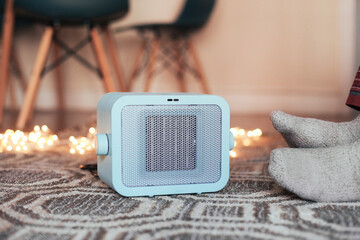 A blue heater on the carpet in a cosy room, feet in socks next to the heater, candid lights