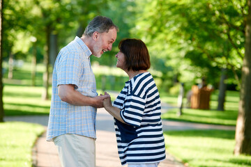 Happy mature wife and husband outdoors. Looking at each other and smiling. Green summer park background.