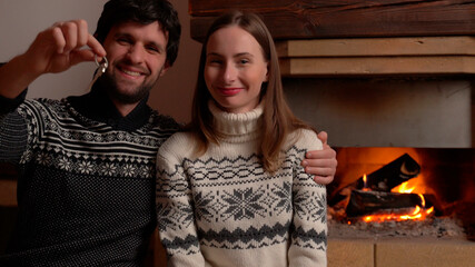 A couple holds a house key in their new home by the fireplace
