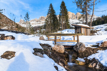Small woodend bridge over a creek in a snowy mountain landscape in the Dolomites on a sunny winter day