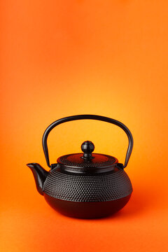 Black cast iron teapot on a orange background.