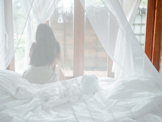 Back view of woman relaxing sitting on bed in mosquito net of an hotel room looking through window in vacations