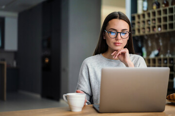 Focused young woman drinking coffee while working with laptop