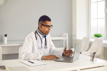 Telemedicine, telehealth and online medicare concept. Young arfican american man doctor making online consultation on laptop with patient during videocall from medical clinic office