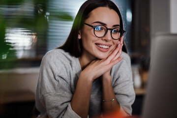 Happy young woman in eyeglasses smiling while working with laptop