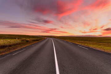 Obraz na płótnie Canvas Deserted road running through medows under a dramatic sky at sunset