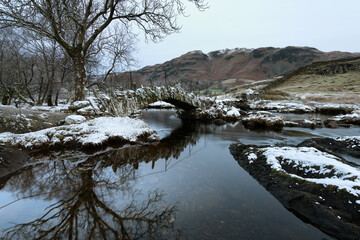 Slaters Bridge in Little Langdale on a cold Winters morning with snow on rocks. Lake District, UK.