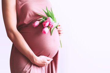 Beautiful pregnant woman with tulips flowers holds hands on belly. Young woman in dress waiting for...