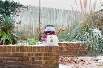 A snowman in a protective mask welcomes the first snow in London in 2021. Winter day during the pandemic coronavirus.