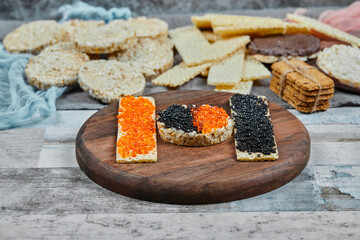 Rice crackers with red and black caviar on a wooden plate