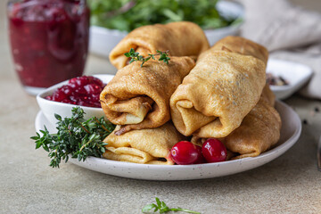 Homemade stuffed thin pancakes or crepes with meat, spicy cranberry sauce and arugula, light stone background. Traditional Russian cuisine for Maslenitsa. Shrove Tuesday.