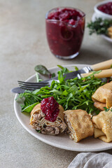 Homemade stuffed thin pancakes or crepes with meat, spicy cranberry sauce and arugula, light stone background. Traditional Russian cuisine for Maslenitsa. Shrove Tuesday.