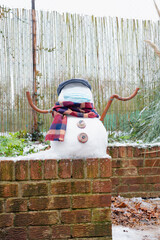 A snowman in a protective mask welcomes the first snow in London in 2021. Winter day during the pandemic coronavirus.