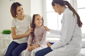 Mother and daughter at the doctor's office. Friendly female practitioner talking to child during health checkup at the clinic. Happy little patient smiling at pediatrician during visit to the hospital