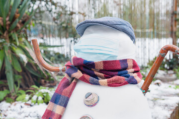 A snowman in a protective mask welcomes the first snow in London in 2021. Winter day during the pandemic coronavirus.