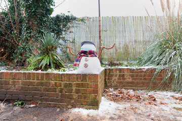 A snowman in a protective mask welcomes the first snow in London in 2021. Winter day during the pandemic coronavirus.