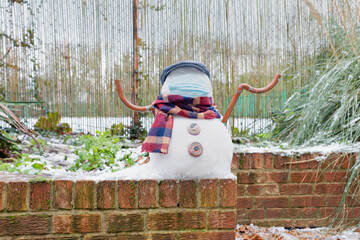 A snowman in a protective mask welcomes the first snow in London in 2021. Winter day during the pandemic coronavirus.