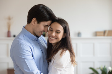 Close up happy young couple hugging, smiling woman and man enjoying tender moment, standing at home, happy attractive wife and husband touching foreheads, expressing love and care, romantic date