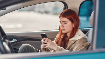 Portrait of teenage girl looking focused at the screen while using her phone, sitting in the car