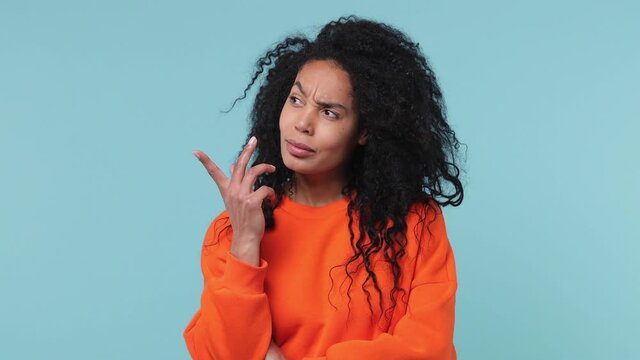Puzzled pensive thoughtful young african american woman 20s years old in basic casual orange sweatshirt look aside up put hand prop up on chin isolated on pastel blue color background studio portrait