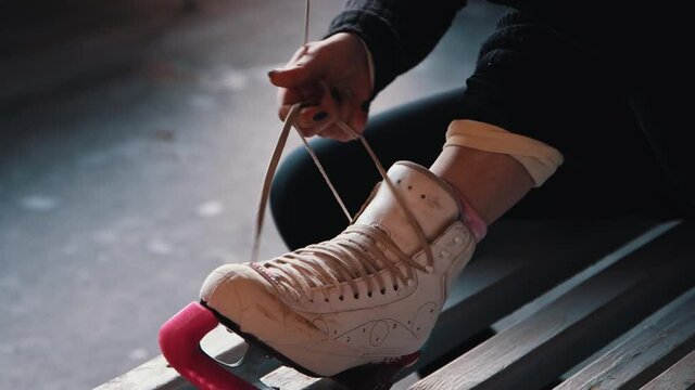 A young woman ties shoelaces on white skates 