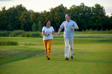 Fototapeta premium Happy couple holding hands and walking. Green lawn field.