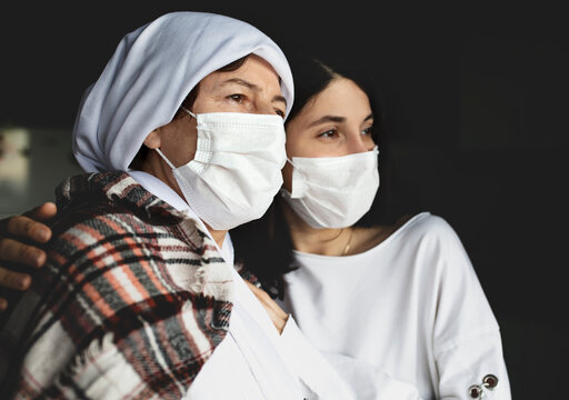 Portrait of senior woman and daughter with facial mask at home. Hopeful old woman waiting for coronavirus vaccine. patient care at home.
