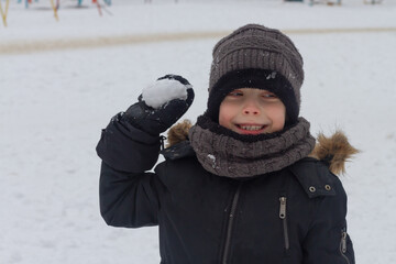 Fototapeta na wymiar A preschool boy in winter clothes aims a snowball in the winter. A child can play snowballs in winter