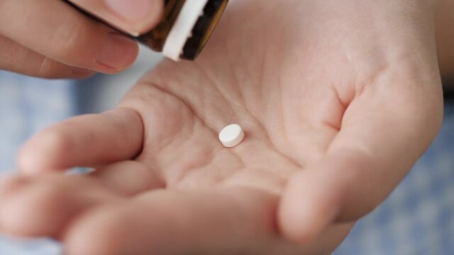 Two small white round pills fall into palm of hand from pill bottle. Close-up, front view, center composition