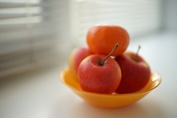red apples and tangerine in an orange plate on the windowsill
