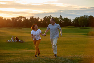 Happy smiling couple holding hands and running. Green field background.