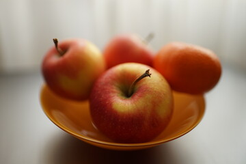 tangerine and three red apples in orange plate on the silver table