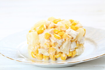 Salad with chicken, pineapple and corn with champagne on a white plate