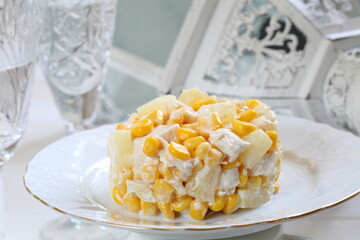 Salad with chicken, pineapple and corn with champagne on a white plate