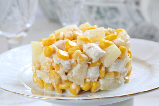 Salad with chicken, pineapple and corn with champagne on a white plate