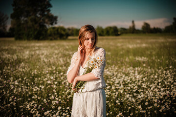 Fototapeta na wymiar Young fashionable woman holding bunch of daisies in her hands wearing a lace playsuit in the middle of daisy meadow