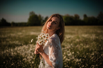 Young blonde woman posing with bunch of daisies in her hands in the middle of a daisy meadow