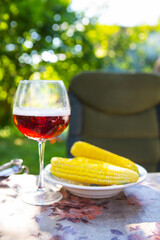 A glass of dark beer in a glass along with a plate of boiled corn, standing on the table. Summer picnic, beautiful sunshine.