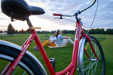 Old red bicycle on the grass. Happy mature couple relaxing on the lawn.