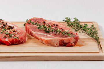 fresh chopped raw pork steaks with spices and thyme on a cutting kitchen board on a white wooden table