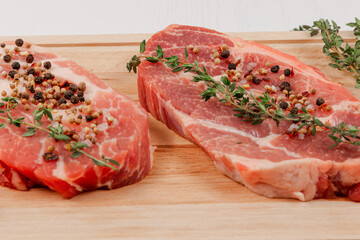 fresh chopped raw pork steaks with spices and thyme on a cutting kitchen board on a white wooden table