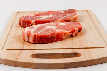 fresh raw marbled pork steak on a solid beech wood cutting board on a white table