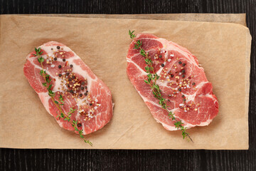fresh raw marbled meat pork steak with thyme on brown parchment paper on a black table. view from above