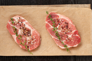 fresh raw marbled meat pork steak with thyme on brown parchment paper on a black table. view from above