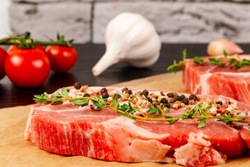 freshly chopped raw pork steaks with spices and thyme on a sheet of parchment. next to ripe red tomatoes and garlic