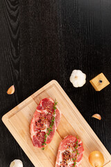 fresh chopped raw pork steaks with spices, garlic and thyme on a cutting kitchen board on a black...