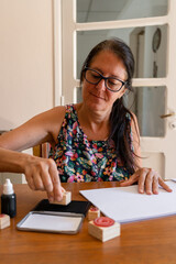 Middle-aged woman putting a decorative stamp on a sheet of paper. Vertical shot.