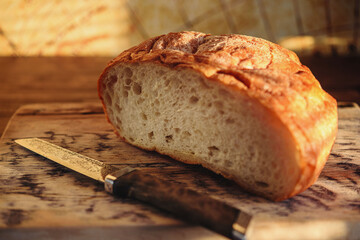 Freshly baked round bread with a golden crust on wooden cutting board. Selective focus